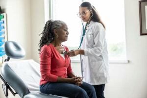 Female doctor listening to senior woman's heart in exam room